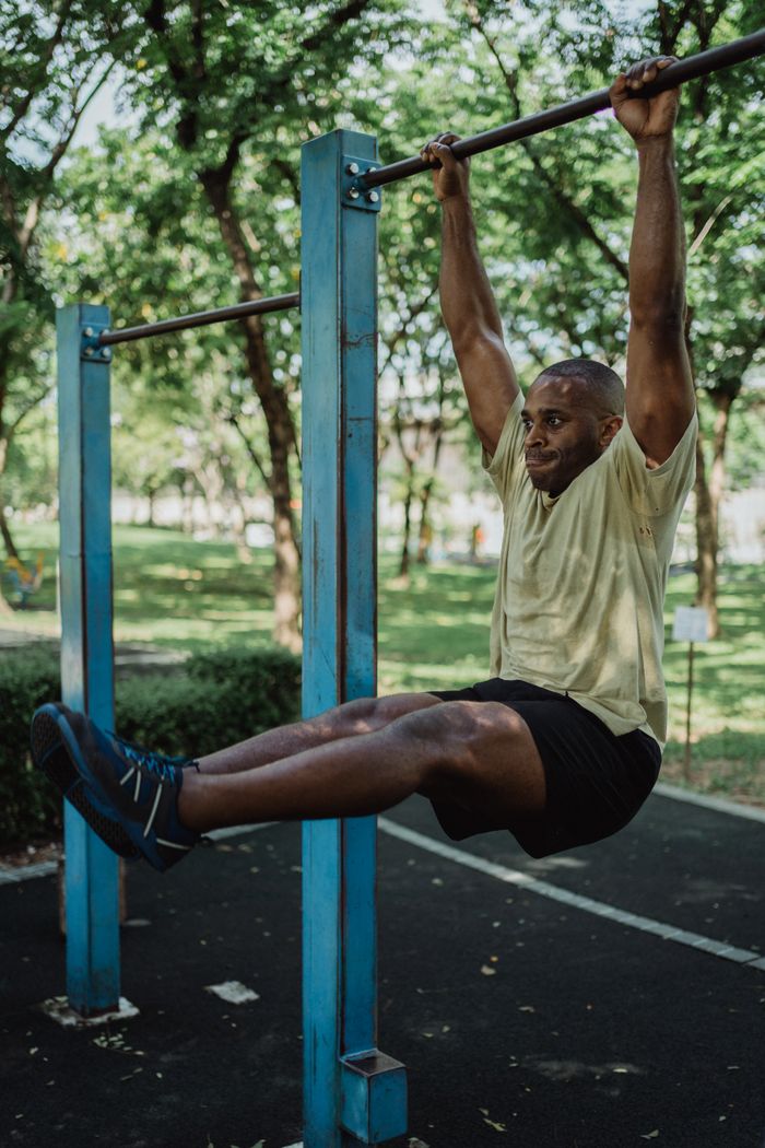 African American man performing hanging exercise on a metal bar in a park.
