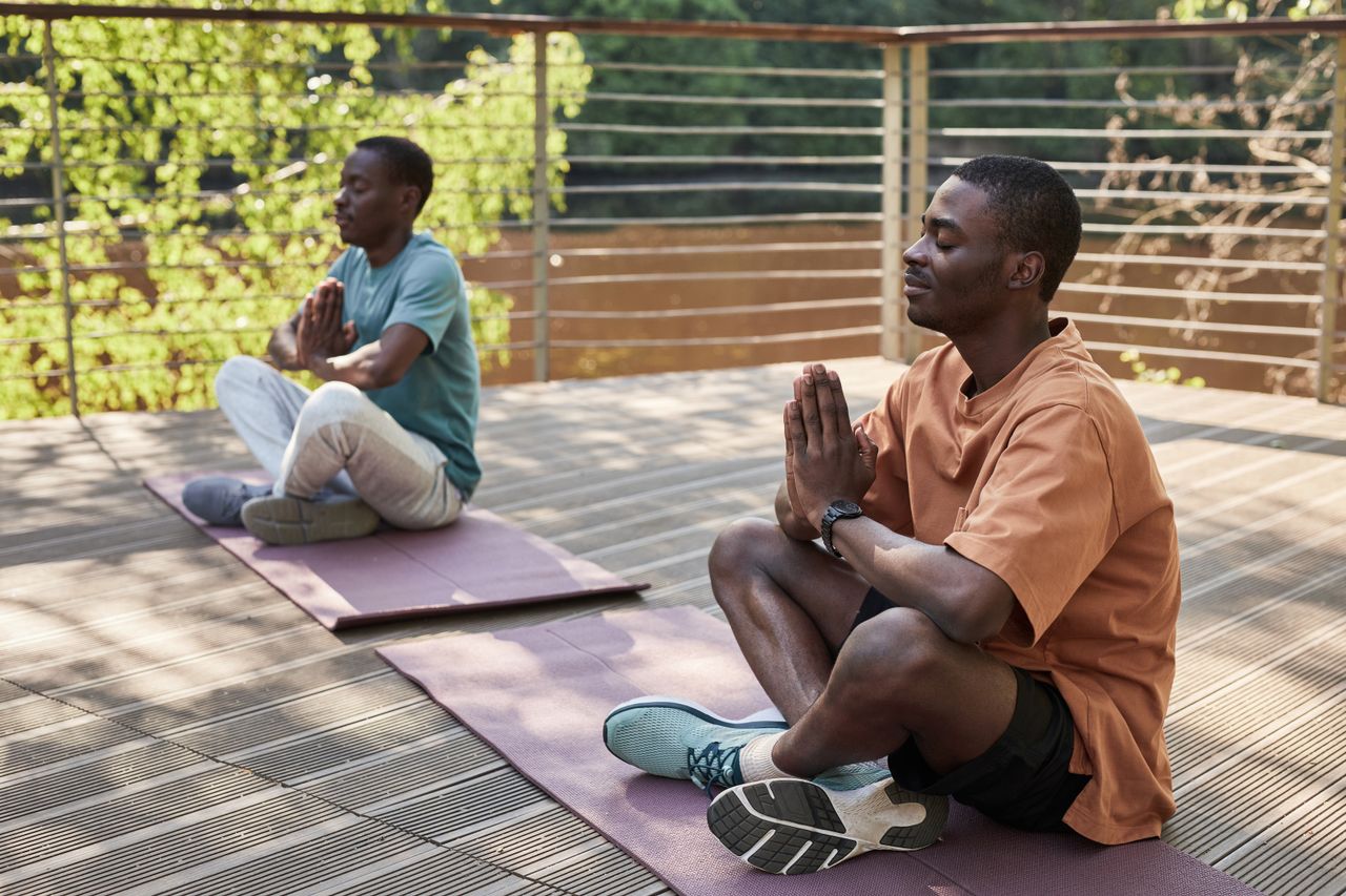 Two men meditating outdoors on yoga mats in a serene setting.
